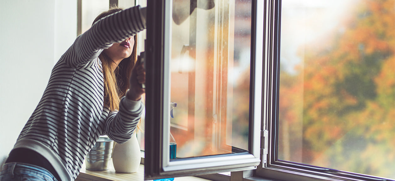 Woman cleaning windows during fall cleaning for air quality.