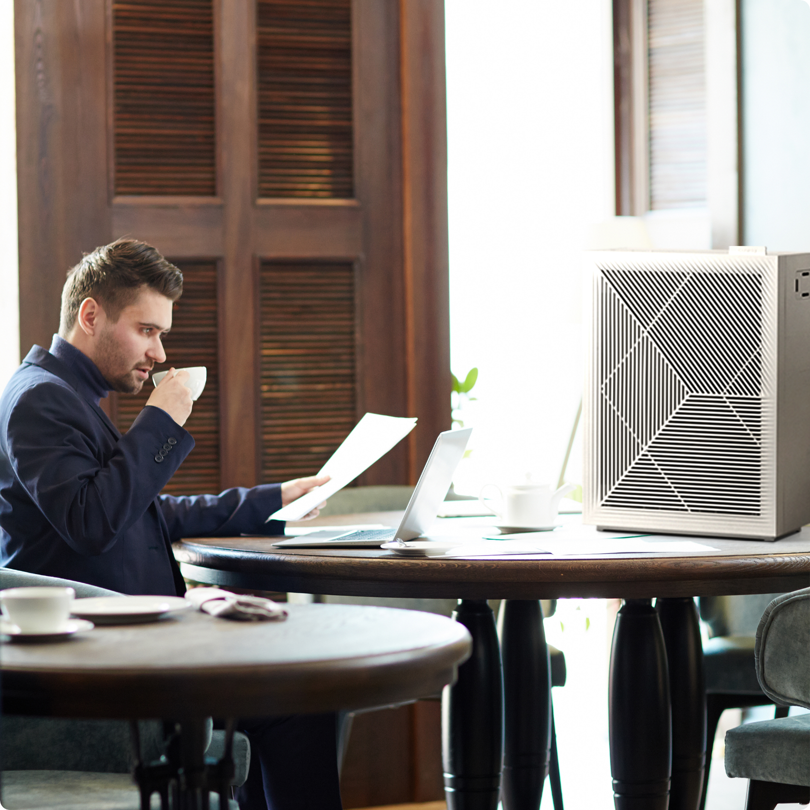 Man sitting at desk & drinking coffee near Airmega air purifier