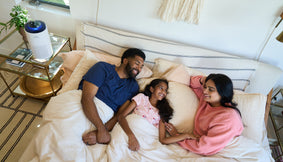 A family in bed next to an air purifier.