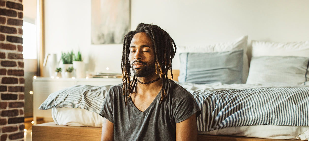 man with eyes closed in front of bed