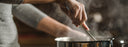 Hand stirring a pot with steam coming off of it