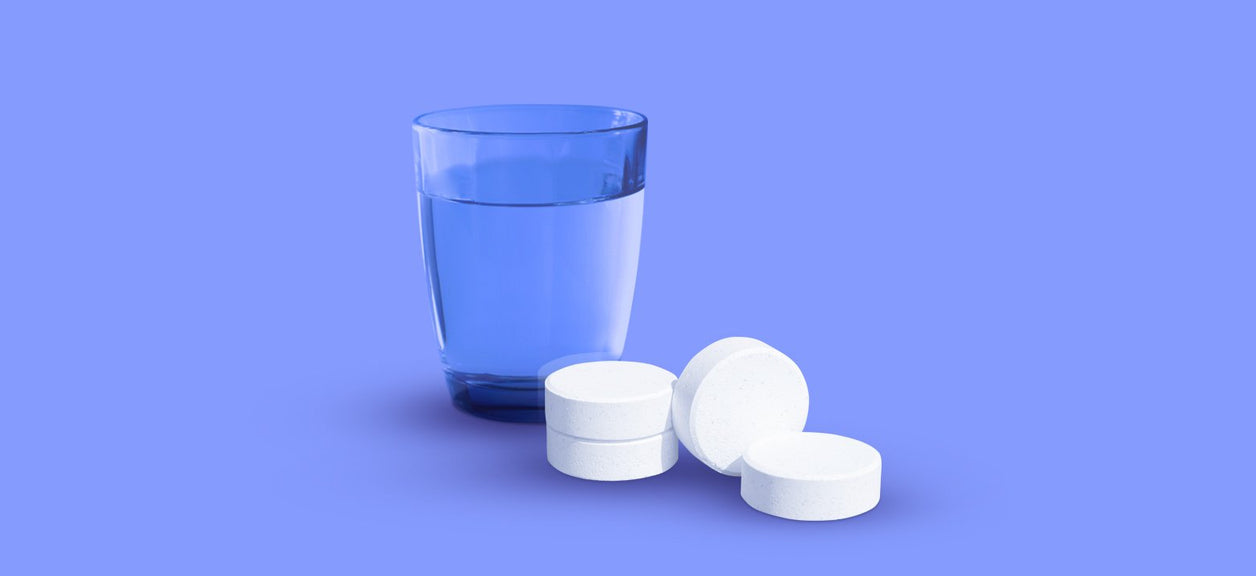 chlorine tablets next to glass of water on purple background