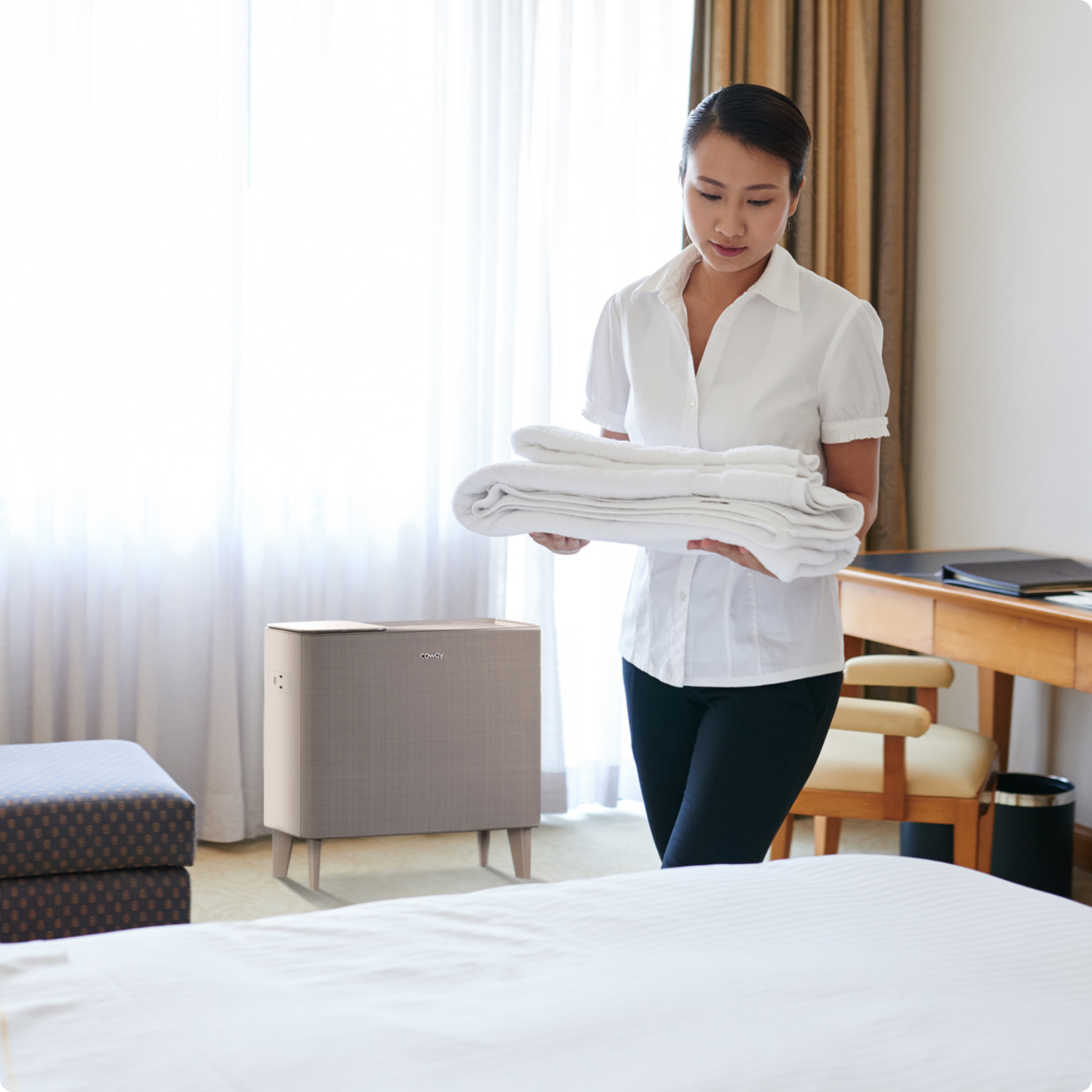 Housekeeper delivering fresh sheets to hotel room with Airmega air purifier