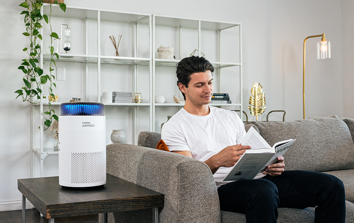 A man is reading a book next to Airmega 100 in the living room